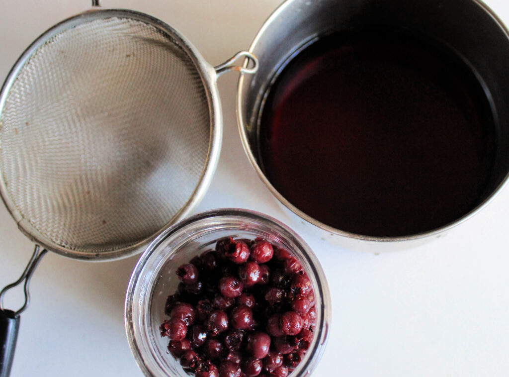 a strainer and pan of juneberry juice and berries showing how to can juneberries